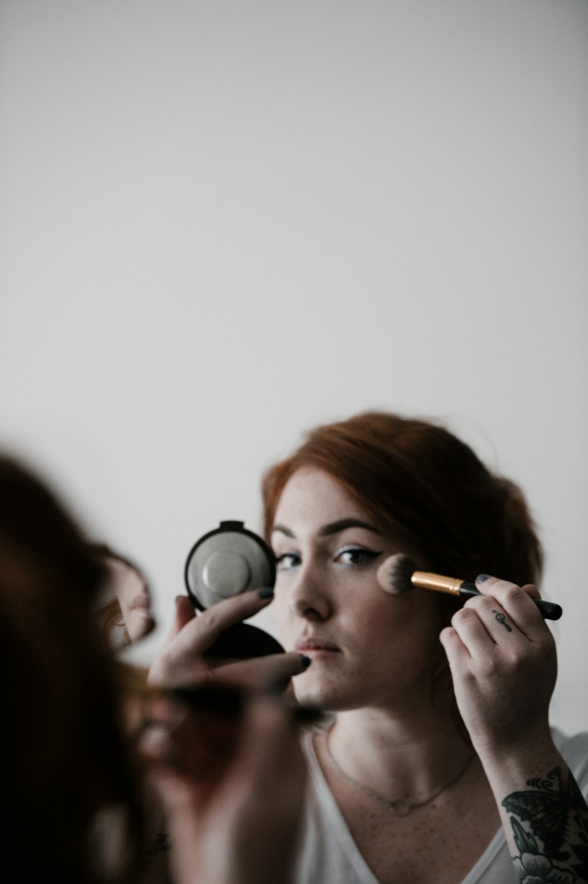 Woman applying liquid foundation with a damp sponge at a bright bathroom mirror in the morning
