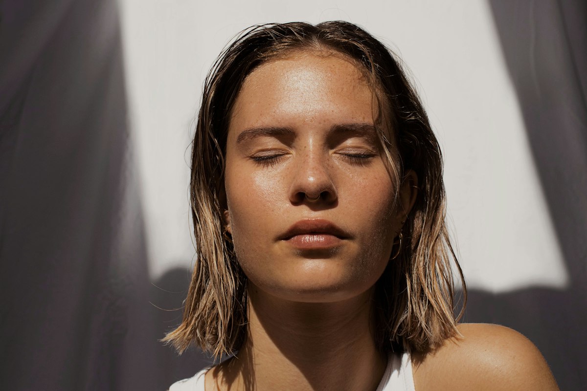 Woman pressing a cotton pad with exfoliating toner to her cheek during her evening routine, skin looking fresh and calm