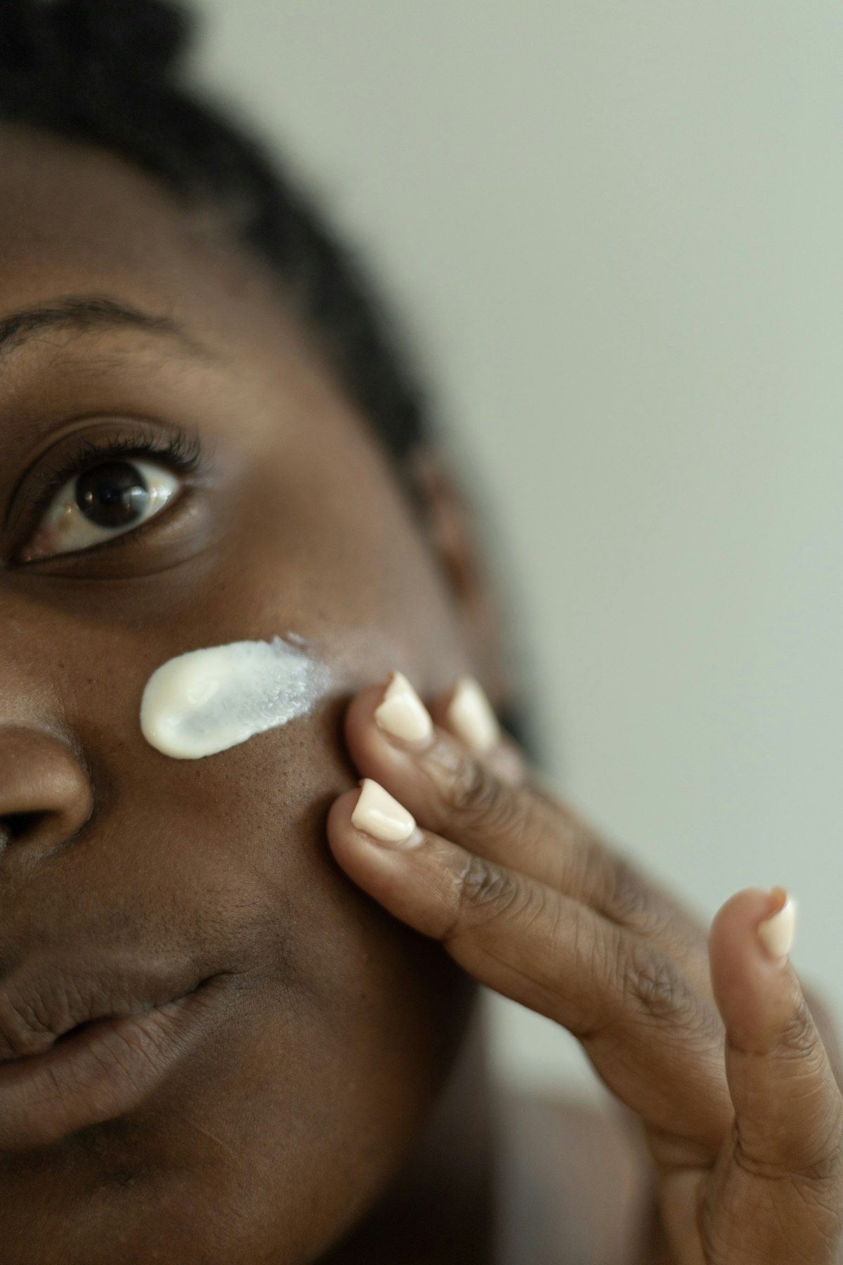 Young woman touching up her face at her office desk mid-morning, gel moisturizer and blotting papers beside her keyboard