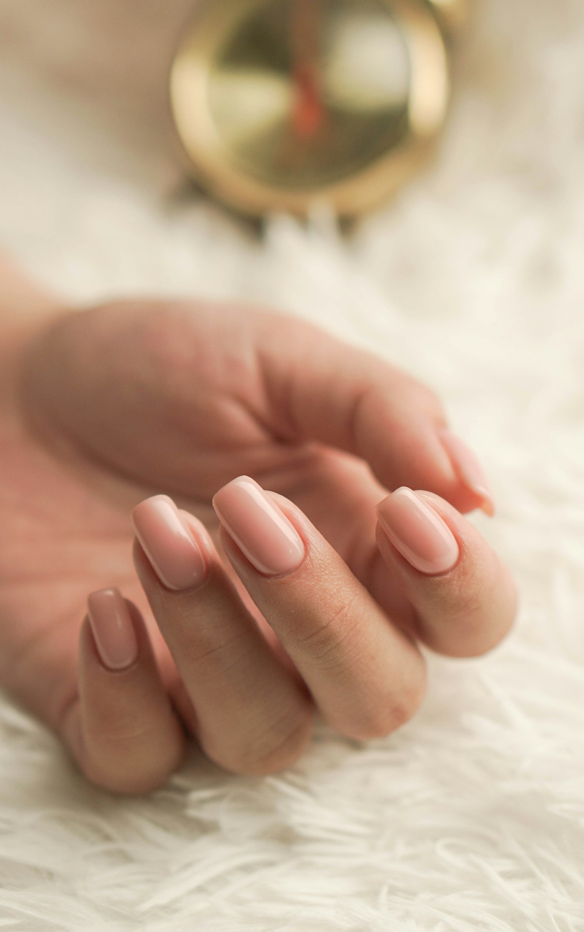 Row of nude nail polish bottles in shades from pale pink to deep cocoa beside a model's hand
