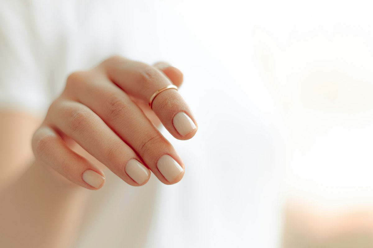 Beginner nail care essentials on a bathroom counter: glass file, cuticle oil, and hand cream